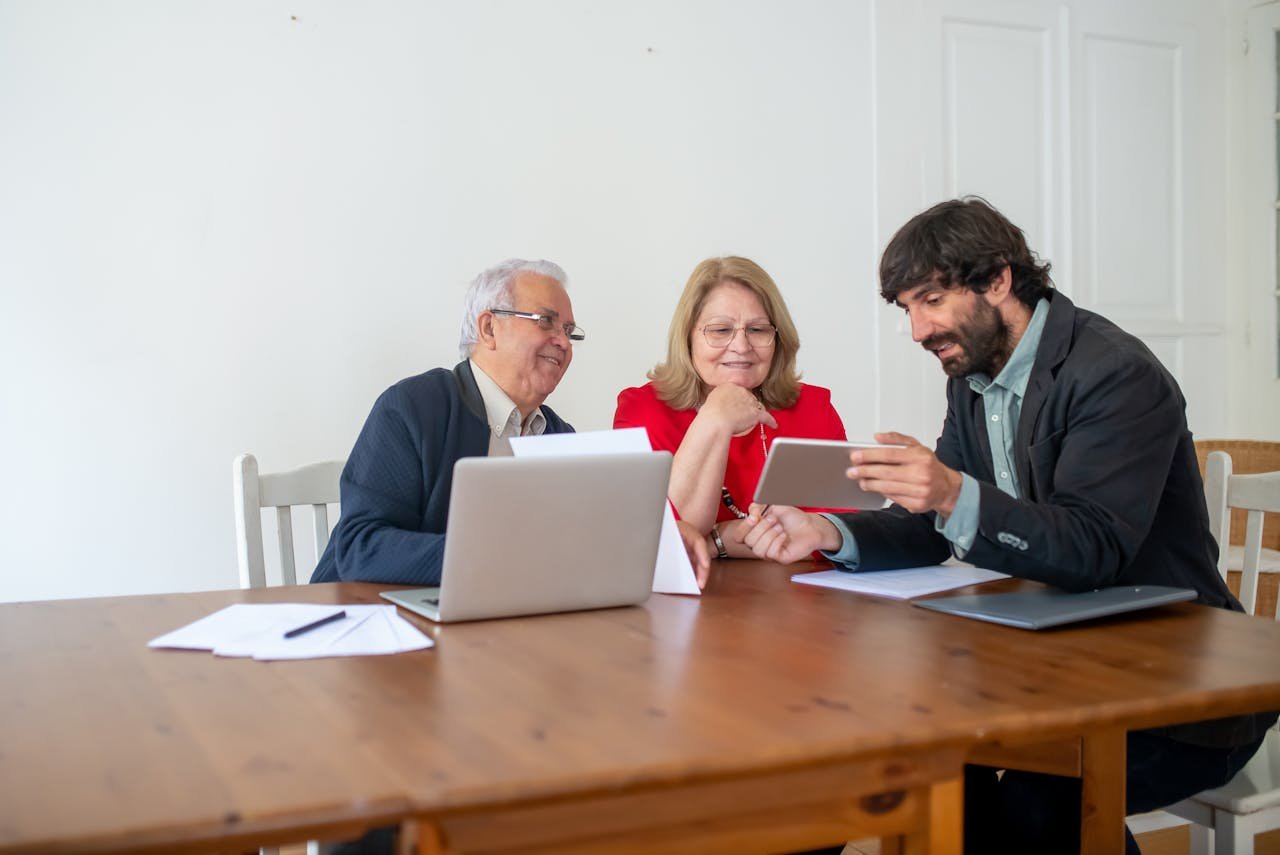 Offerings Two senior clients and a consultant discussing documents and using a tablet in a modern office.